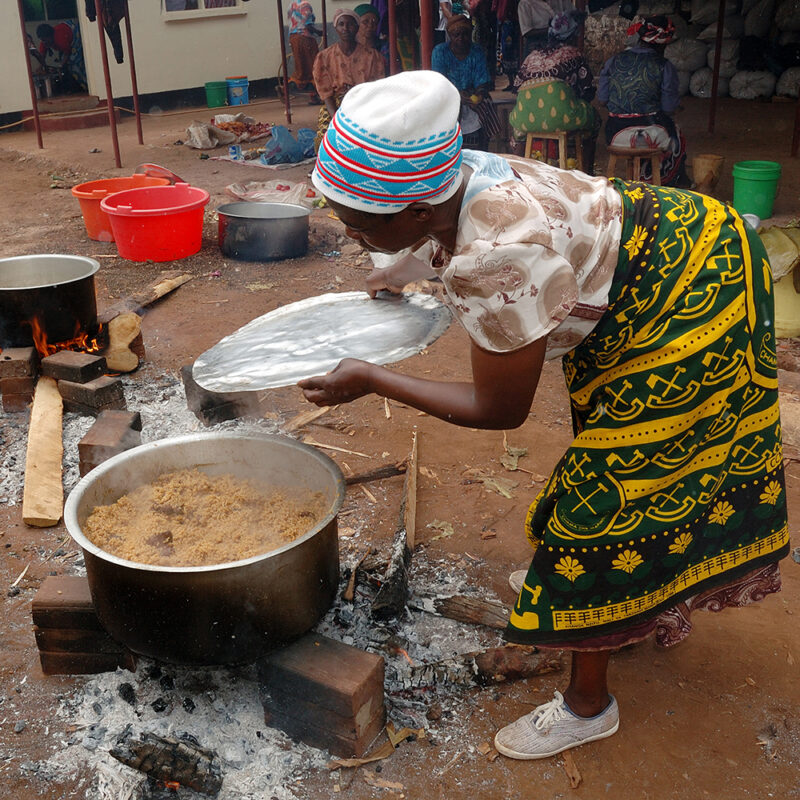 Tanzania, A Tanzanian woman cooks Pilau rice dish wearing traditional Kanga.
